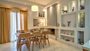 Un espace de salle à manger moderne, avec une table et des chaises en bois, un lustre et des étagères décoratives où sont exposés divers objets.