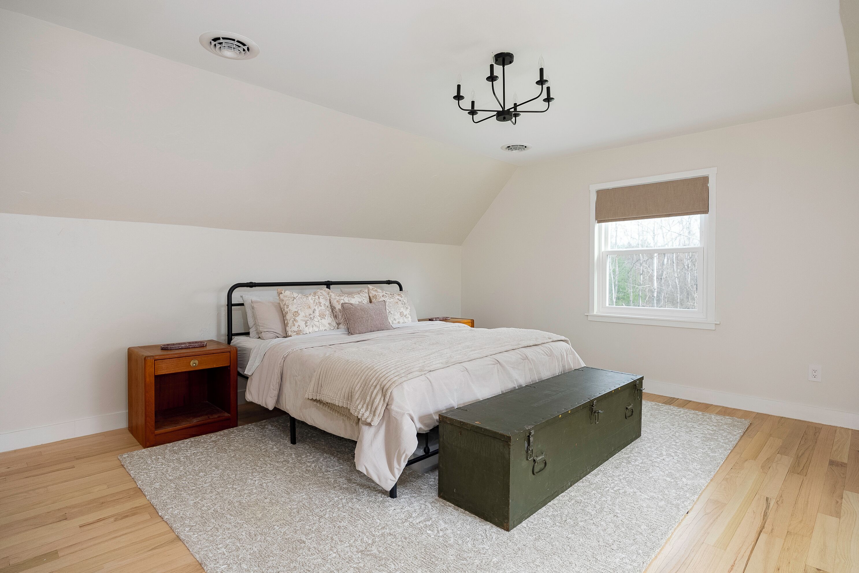 Een slaapkamer met een bed, nachtkastje, bankje en een raam met uitzicht.
