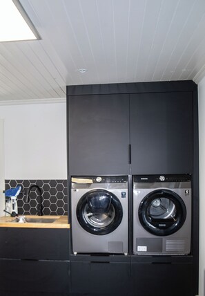 A modern laundry room with two front-loading washing machines, a wooden countertop, and a hexagonal tile backsplash. - Luxury Home with Hot tub close to Killarney Town Centre (KY)