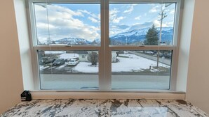 Quarto com uma janela ampla que oferece vista para uma paisagem nevada e montanhas.