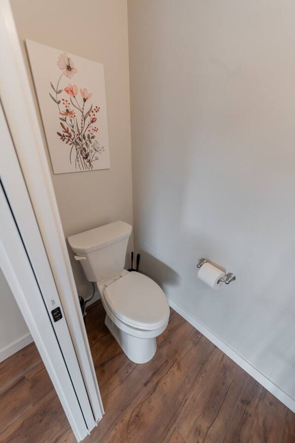 A bathroom with a toilet, a toilet paper holder, and a floral artwork on the wall.