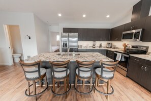 A modern kitchen with a central island, bar stools, stainless steel appliances, and dark cabinetry.
