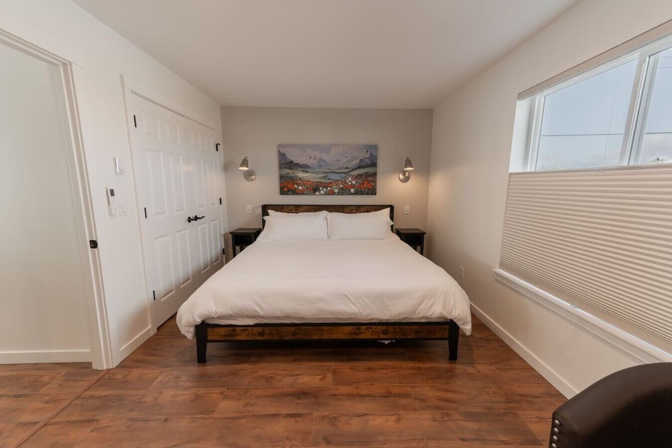 A bedroom with a bed, a painting on the wall, a window with blinds, and a door.
