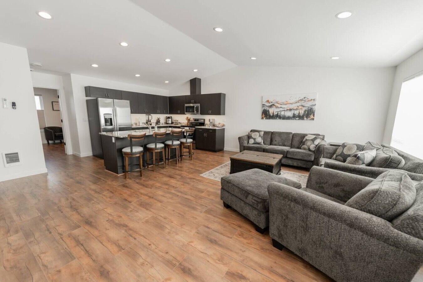A spacious living area with a kitchen island, grey sofas, and a large window.