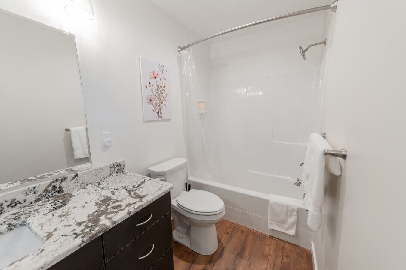 Une salle de bain avec un comptoir en marbre, des toilettes, une baignoire avec un rideau de douche et un plancher en bois.