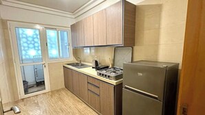 A compact kitchen with wooden cabinets, a stainless steel refrigerator, and a gas stove. - 2 Bedroom Apartment Sea View 🌊 + Free Parking | Rabat (Rabat)
