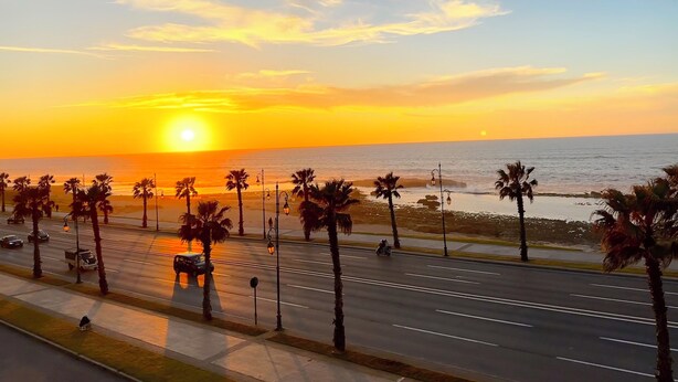 A sunset view with palm trees and a road in the foreground. - 2 Bedroom Apartment Sea View 🌊 + Free Parking | Rabat (Rabat)