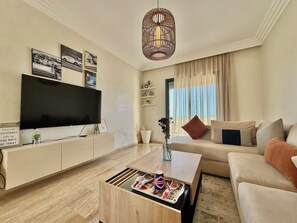 A modern living room with a flat-screen TV, a wooden coffee table, a sofa, and a large window with curtains. - 2 Bedroom Apartment Sea View 🌊 + Free Parking | Rabat (Rabat)