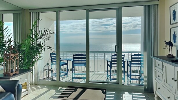 Un balcon avec vue sur l’océan, un coin repas avec des chaises bleues et un buffet blanc.