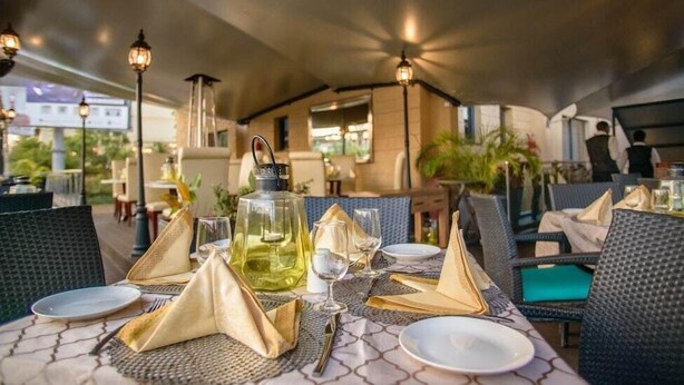 A restaurant setting with tables set for dining, featuring a bottle of olive oil, napkins, and cutlery. - The Landmark Suites (Nairobi)