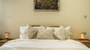 A neatly made bed with patterned bedding and pillows, a wall art piece, and two bedside lamps on nightstands. - The Landmark Suites (Nairobi)