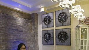 A reception area with a marble counter, multiple wall clocks, and a decorative hanging light fixture. - The Landmark Suites (Nairobi)