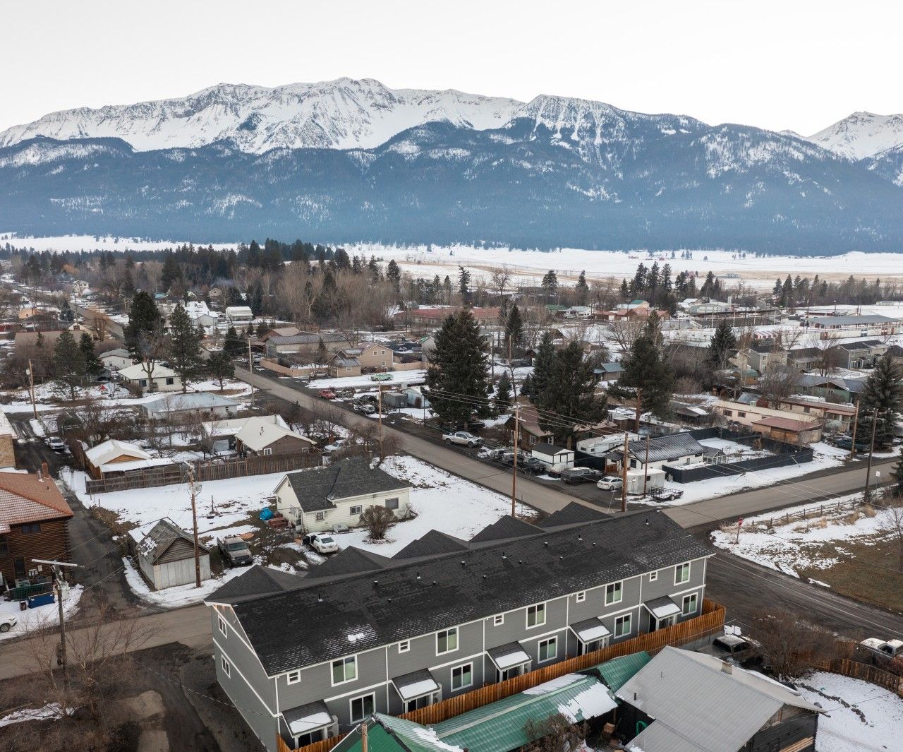 A residential area with a row of townhouses, a green-roofed building, and snow-covered mountains in the background.