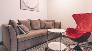 A room with a beige sofa, a small white table, and a red chair. - Aparthotel Fortune (Poznań)