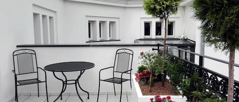 A balcony with a table and two chairs, surrounded by potted plants and a small tree.