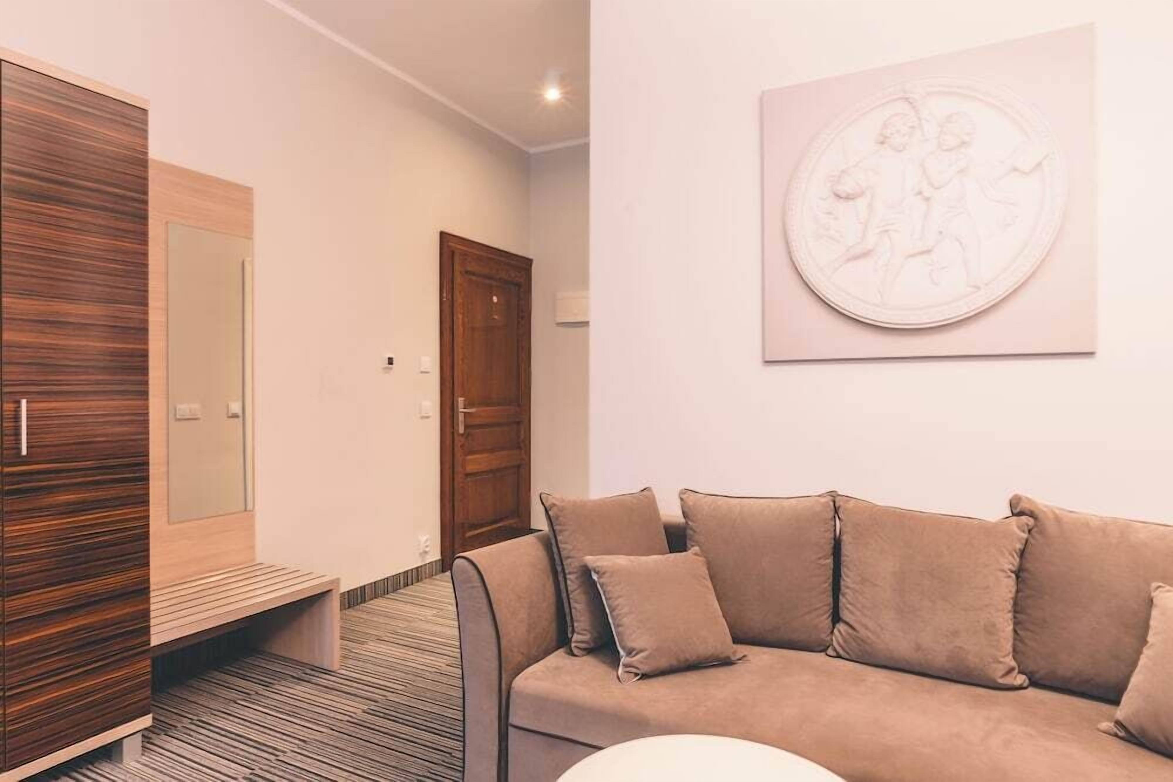 A modern hotel room with a sofa, a wooden wardrobe, a bench, and a wall-mounted artwork.