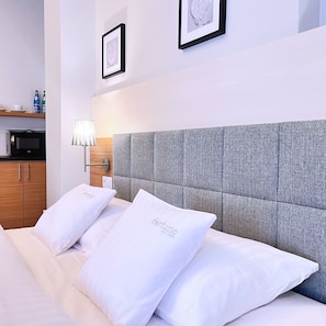 A hotel room with a bed, pillows, a nightstand, a lamp, a microwave, and framed pictures on the wall. - Aparthotel Fortune (Poznań)
