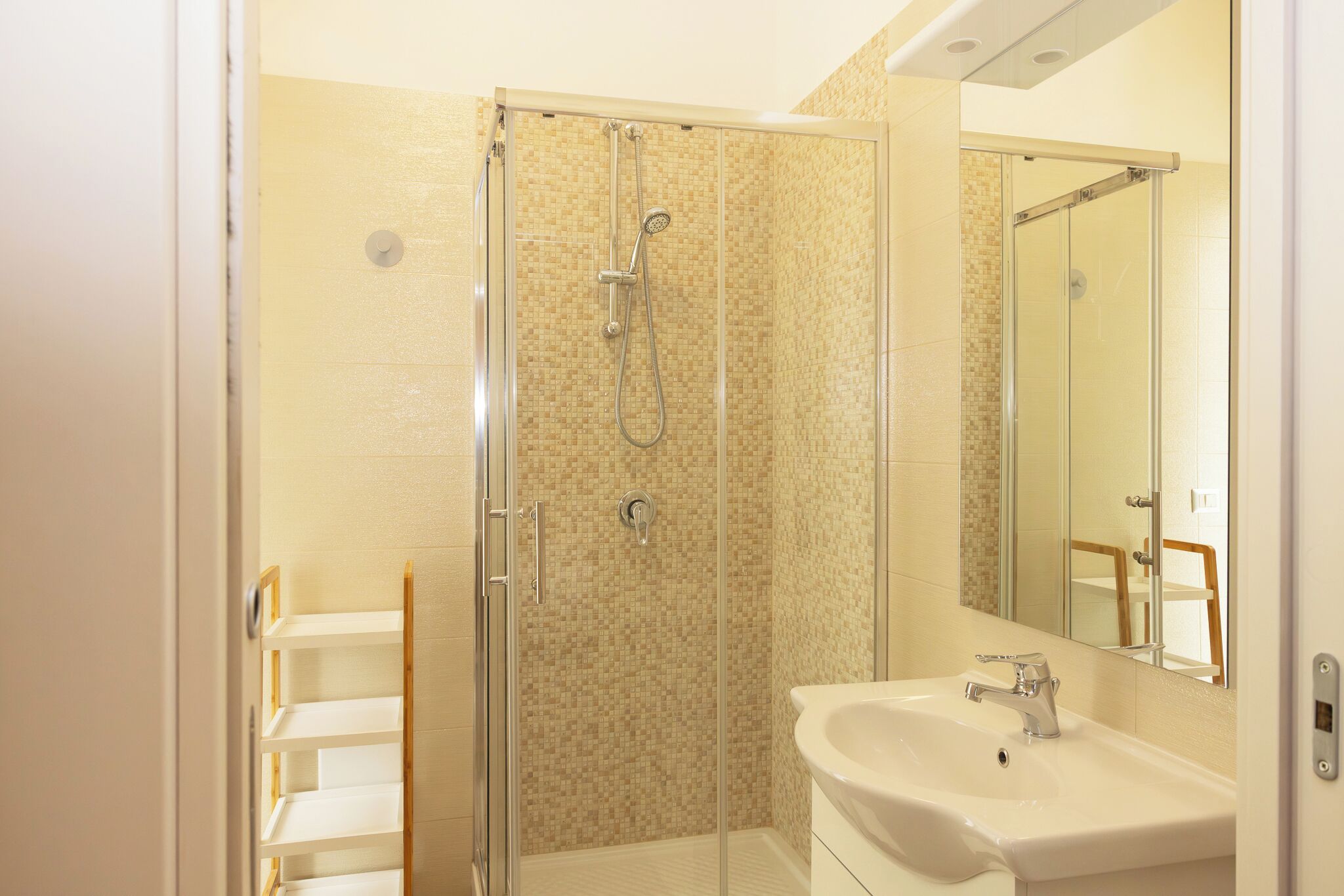 A bathroom with a glass shower enclosure, a sink, and a mirror.