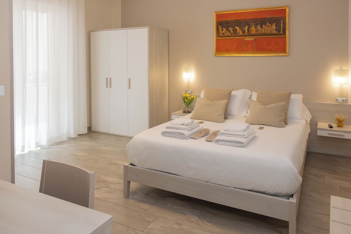 A bedroom with a bed, a wardrobe, a nightstand with a lamp, and a painting on the wall.