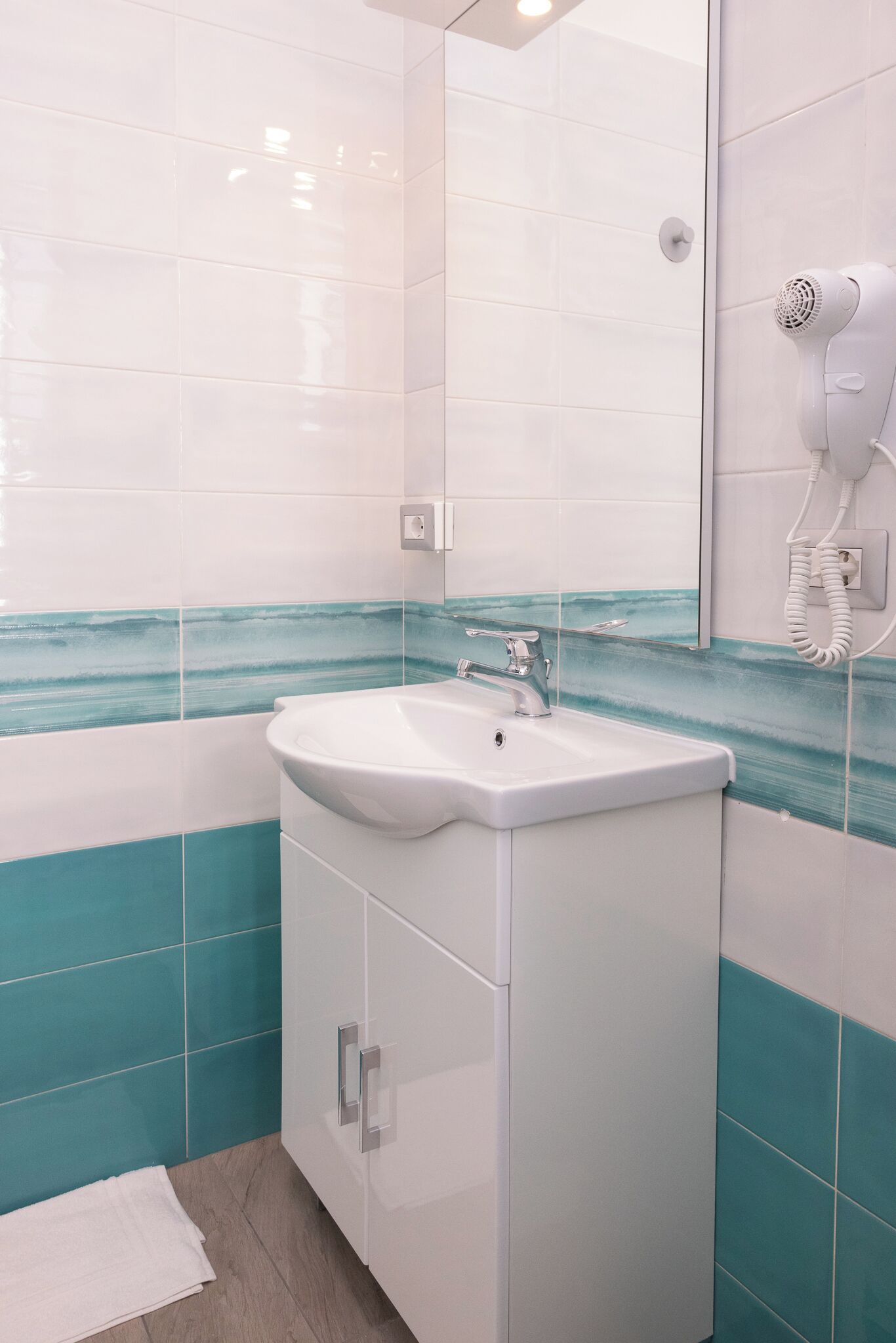 Un baño con azulejos blancos, un lavamanos, un espejo y un secador de pelo.
