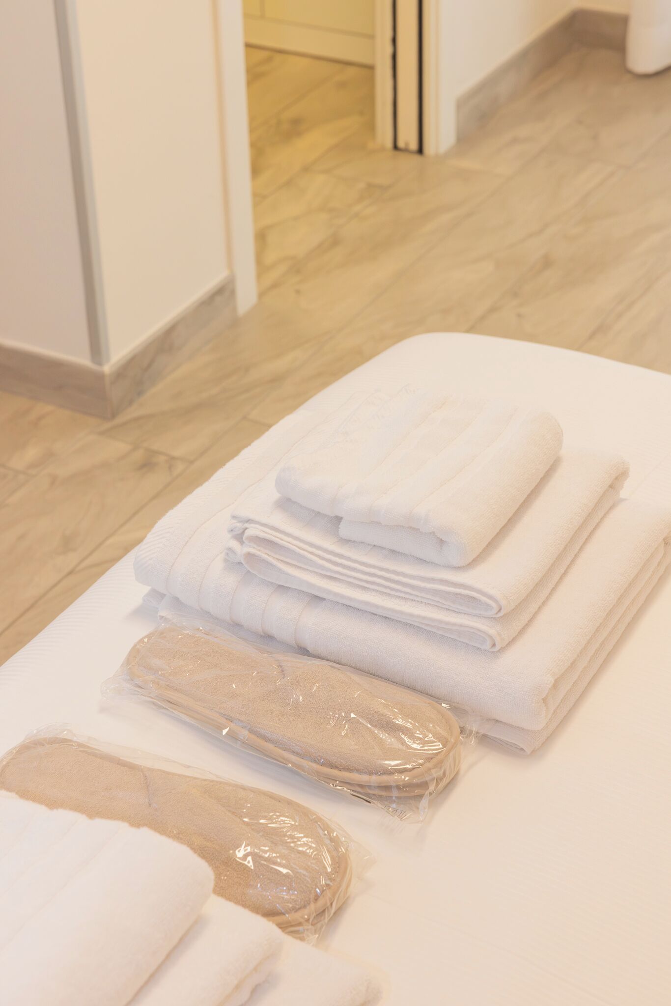 A neatly arranged set of towels and bath mats on a white surface in a room with wooden flooring and white walls.