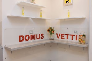 Ein Empfangsbereich mit weißen Regalen, auf denen Flaschen stehen, einer Vase mit Blumen und einem Korb mit Früchten.