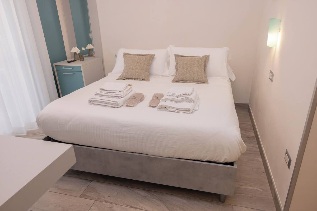 A modern hotel room with a bed, bedside tables, and a nightstand.