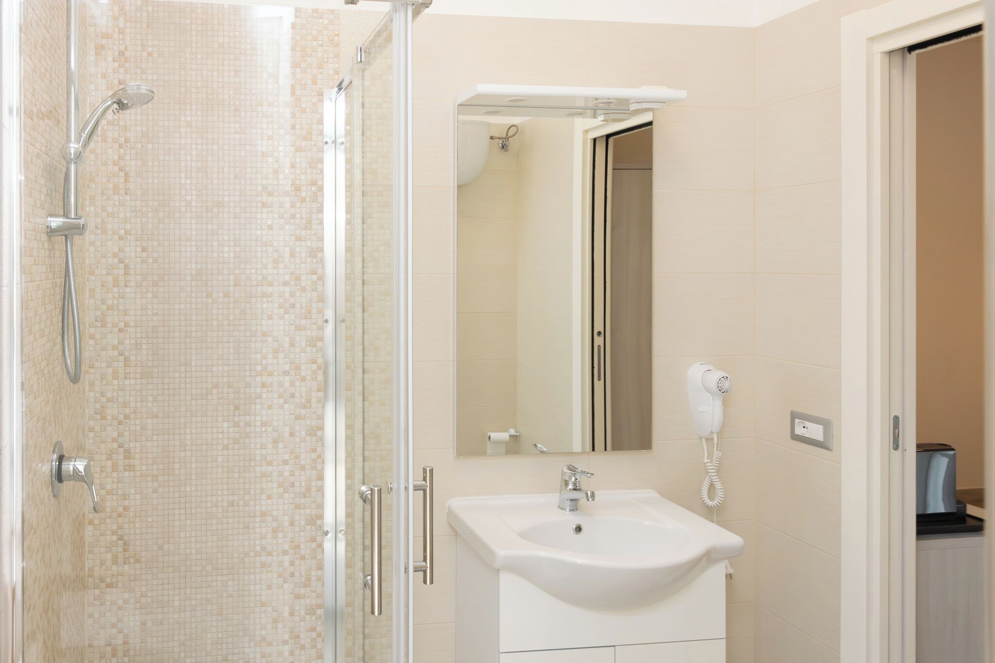A bathroom with a shower, sink, mirror, and hairdryer.