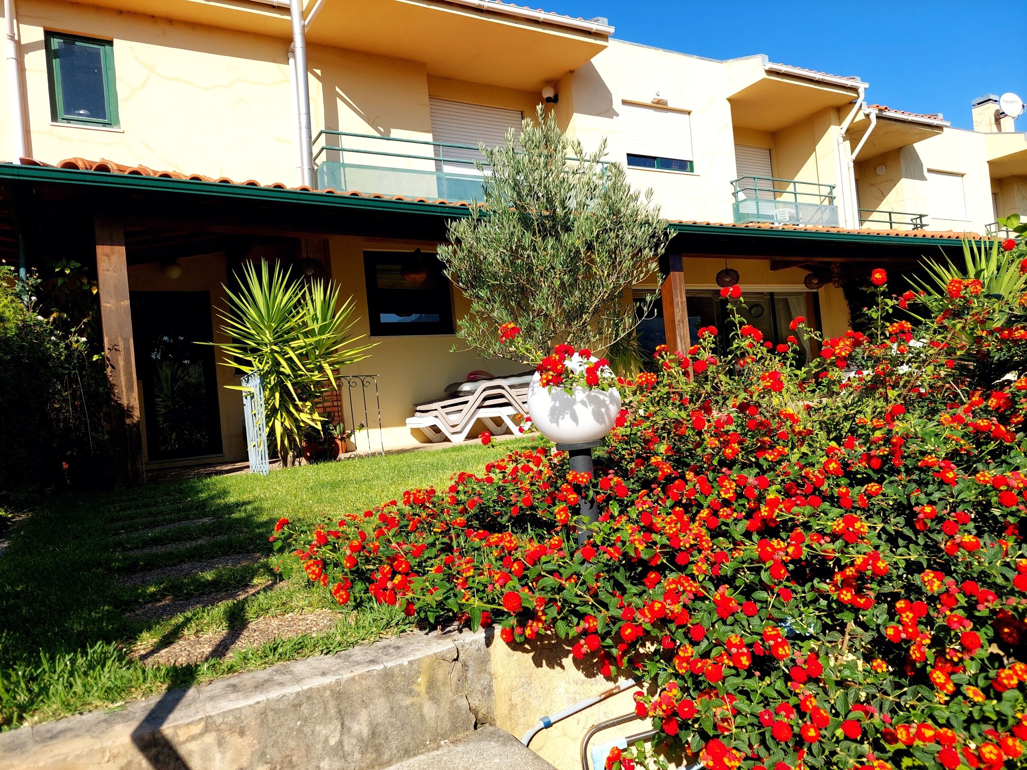 A residential building with a balcony, a garden with red flowers, and a white lamp post.
