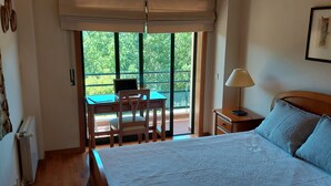 A bedroom with a bed, a desk with a laptop, a chair, a nightstand, and a window with a view of greenery. - DREAM HOUSE at Douro Valley with river view at 30Kms of Porto (PENAFIEL)