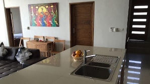 A modern kitchen with a large island, a dining area with wooden furniture, and a colorful abstract painting on the wall. - Air Sanih Beach Villa (Kubutambahan)