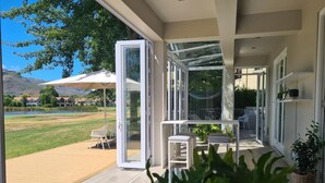 Puerta corredera de vidrio abierta que da a un patio con mobiliario exterior, vista a un lago y una montaña al fondo.