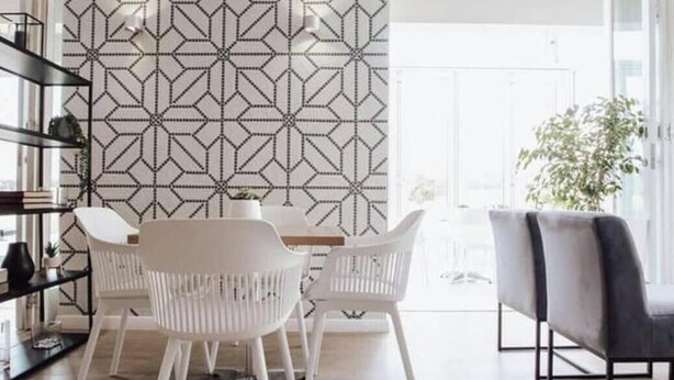 Un interior moderno con una pared de diseño geométrico, una zona de comedor con sillas blancas y un sofá.