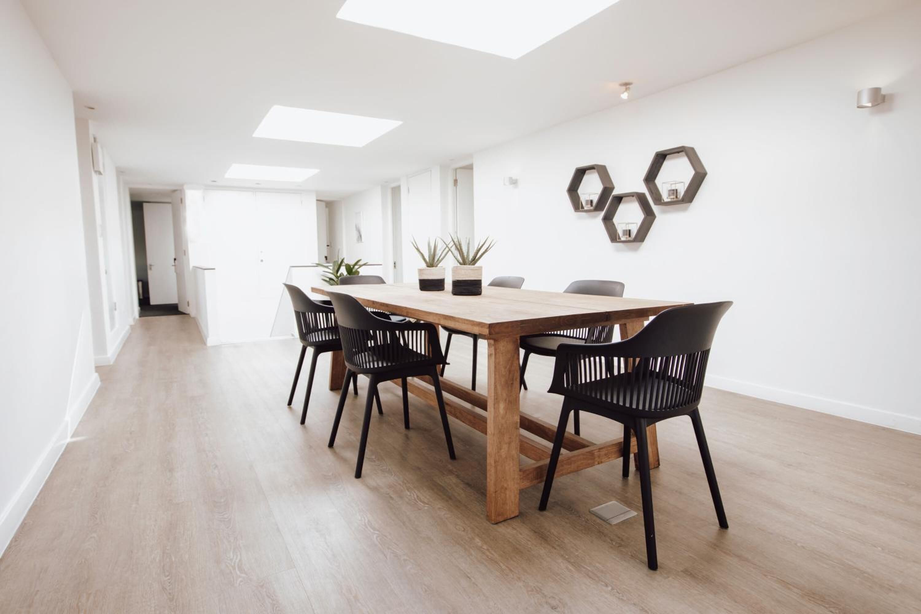 A modern dining area with a wooden table and black chairs, white walls, and hexagonal wall art.
