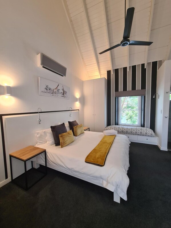 A bedroom with a large bed, a bedside table, a ceiling fan, a window with blinds, and a wall-mounted air conditioning unit. - Boschenmeer Grande Lodge (Paarl)