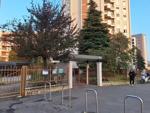 Ein verschlossenes Tor mit einem Metallzaun, einem überdachten Gang und einem hohen Wohngebäude im Hintergrund.
