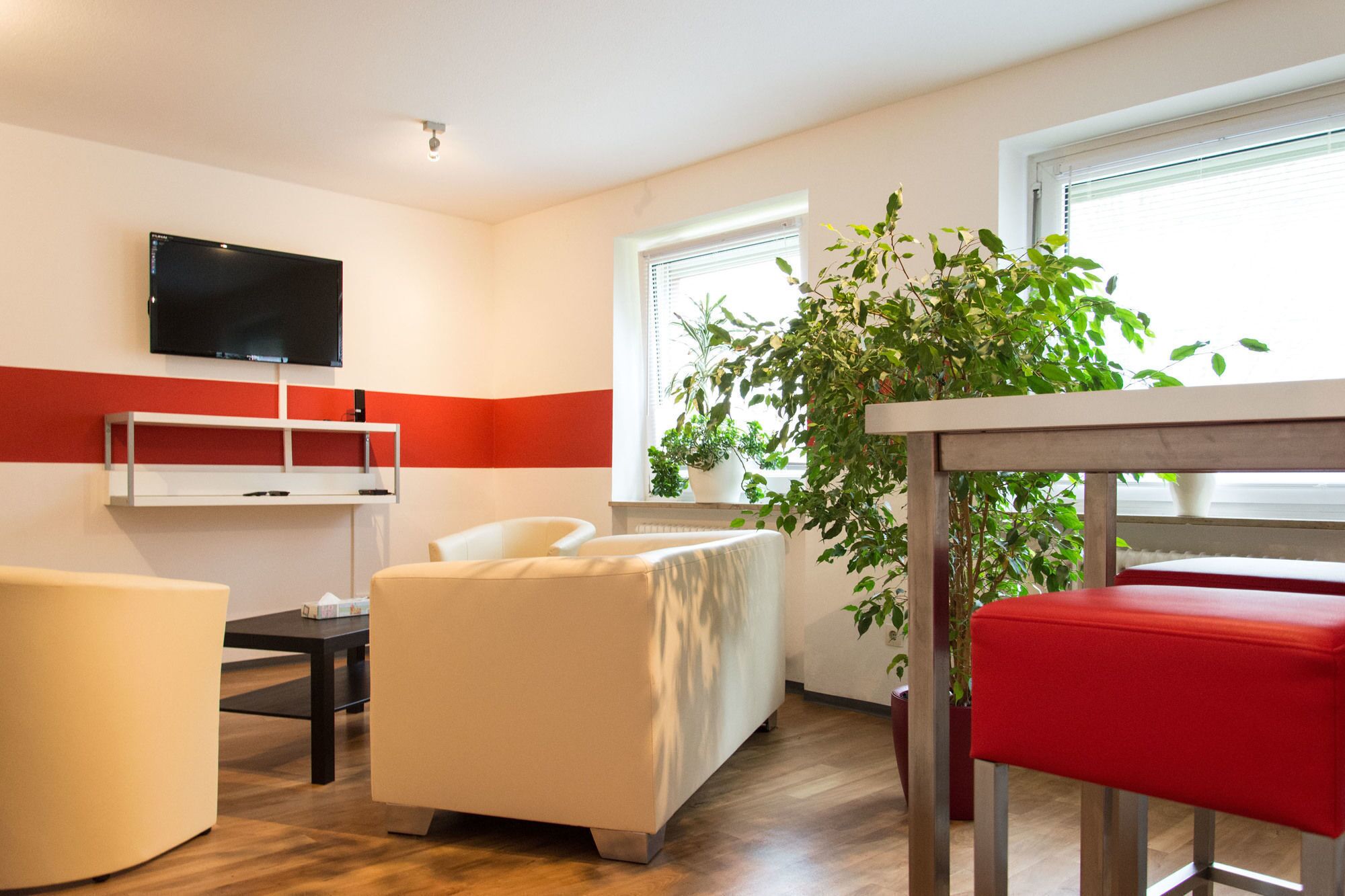 A modern hotel room with a flat-screen TV, a sofa, a dining table, and a potted plant.
