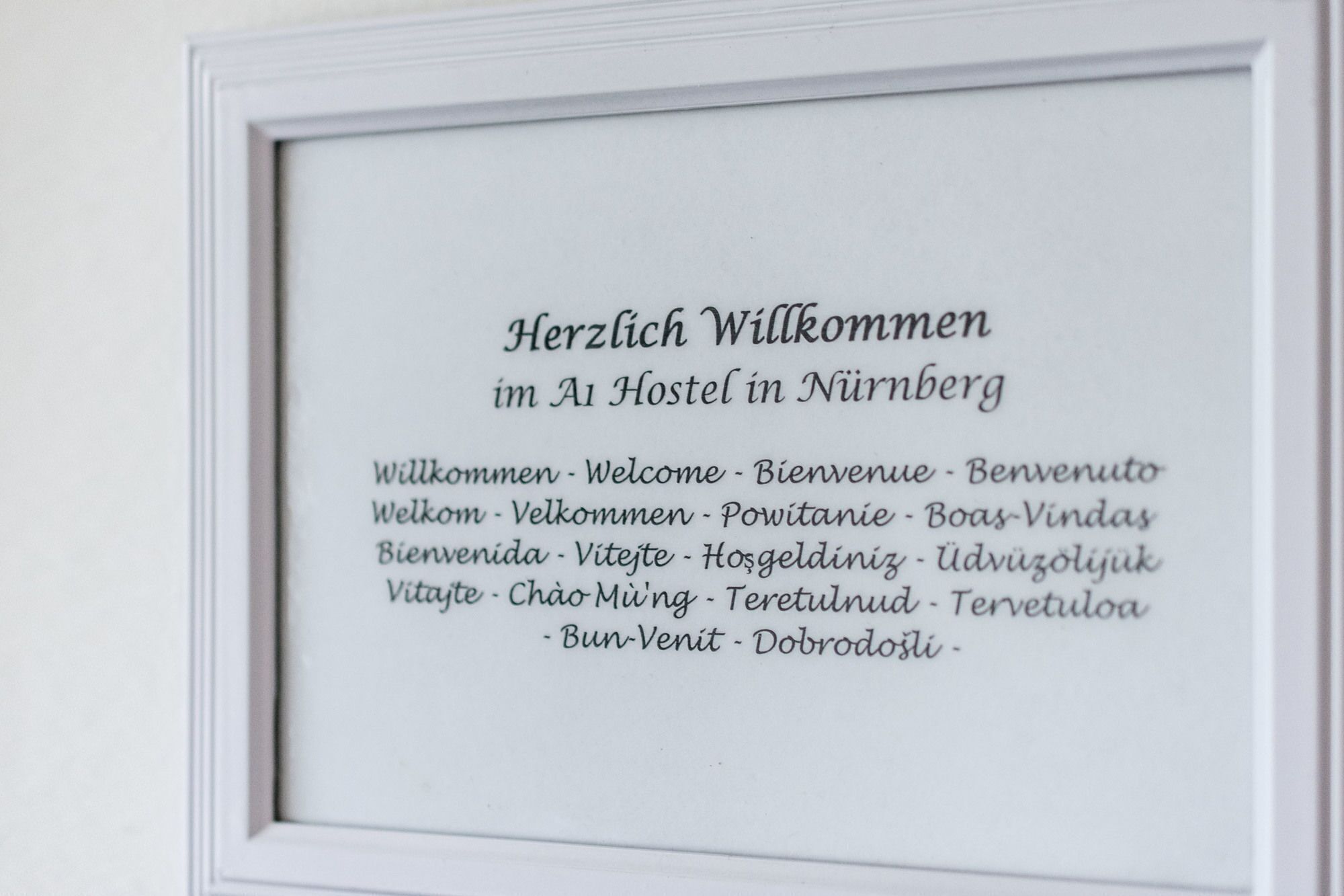 A framed welcome sign with multilingual greetings in a white frame.