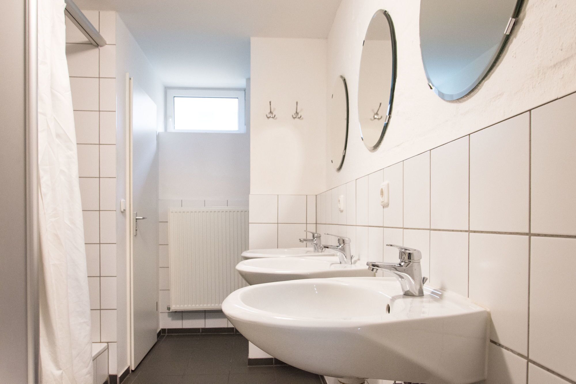 A modern bathroom with three sinks, a window, and a radiator.