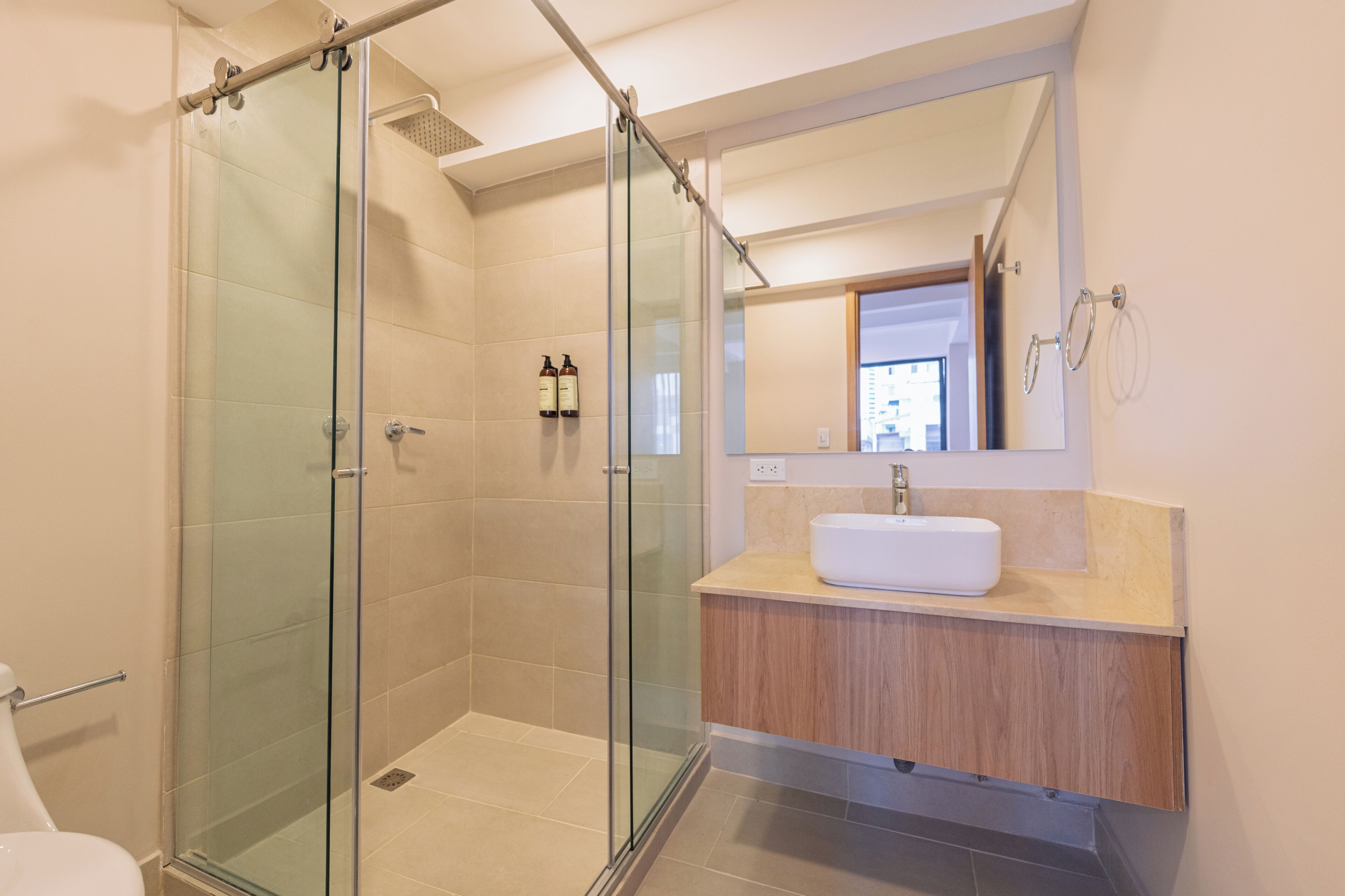 A modern bathroom with a glass-enclosed shower, a white sink, and a wooden vanity.
