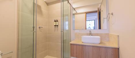 A modern bathroom with a glass-enclosed shower, a white sink, and a wooden vanity.