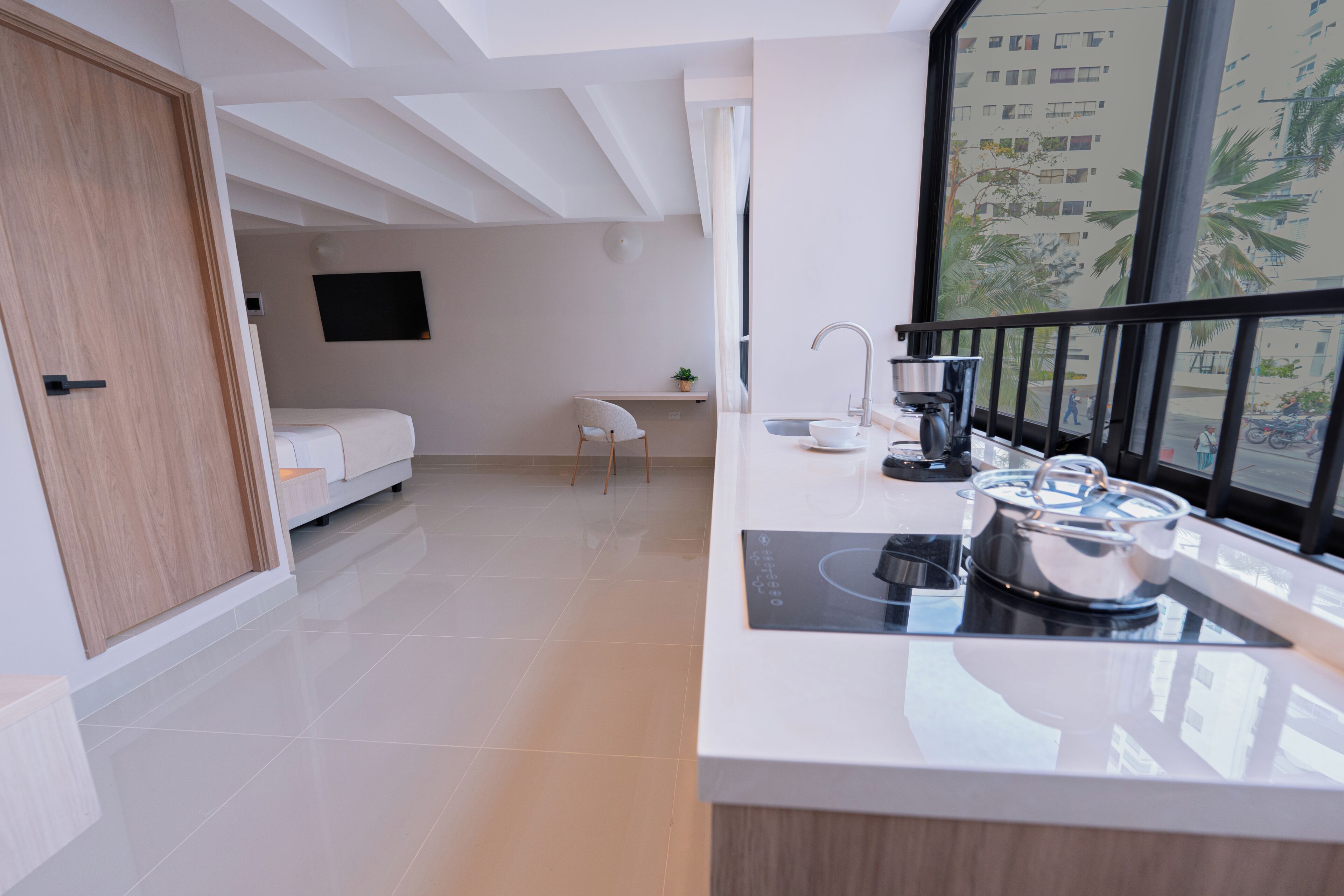 Cozinha moderna com fogão embutido, pia e janela com vista para edifícios e palmeiras.