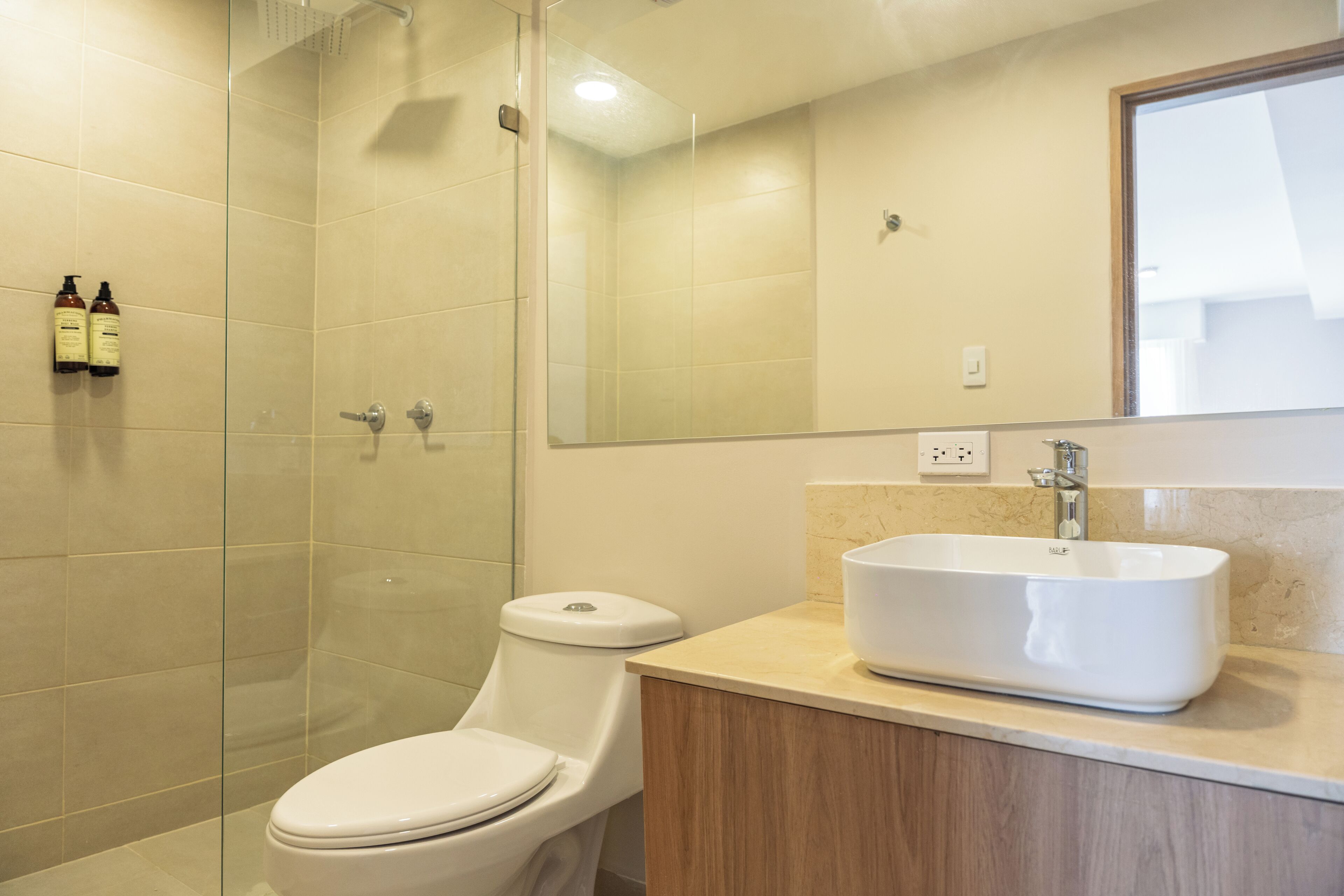 A modern bathroom with a glass shower enclosure, a white toilet, and a beige sink with a mirror above it.