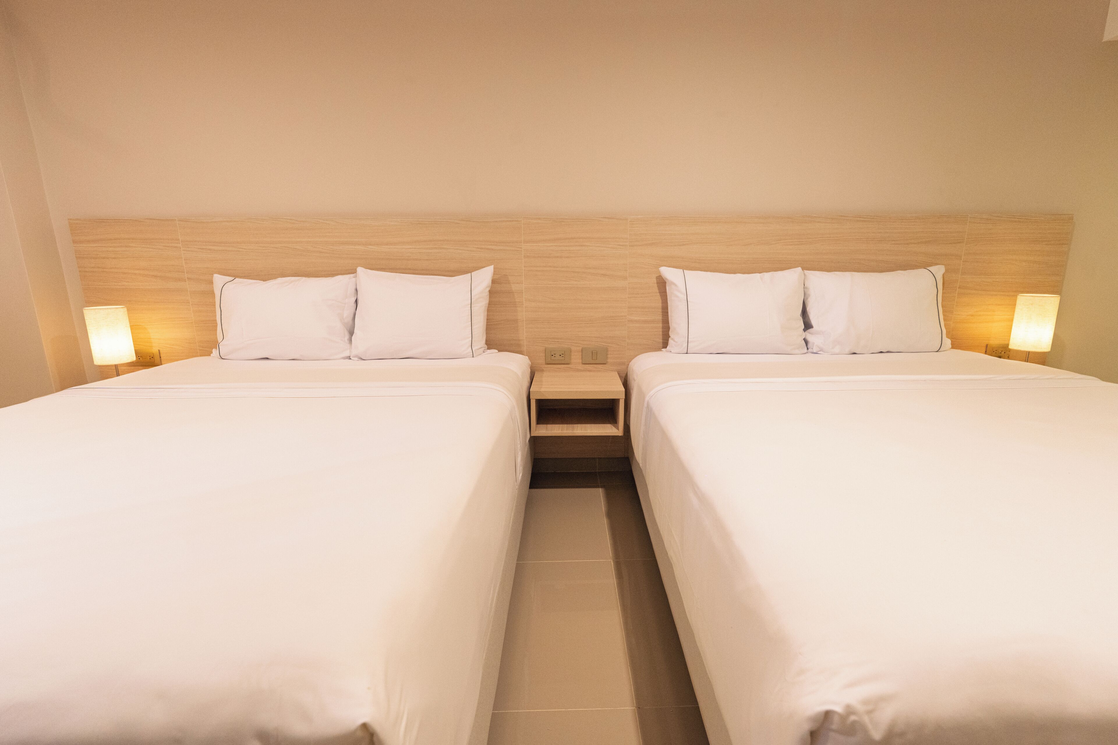 Una habitación de hotel con dos camas, un cabecero de madera, lámparas de noche y una mesita de noche.