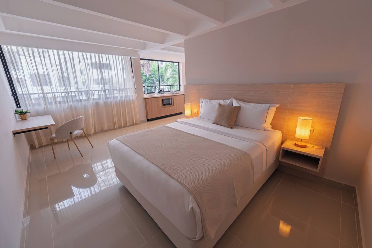 A modern hotel room with a large bed, bedside lamps, a desk, and a view of the outdoors.