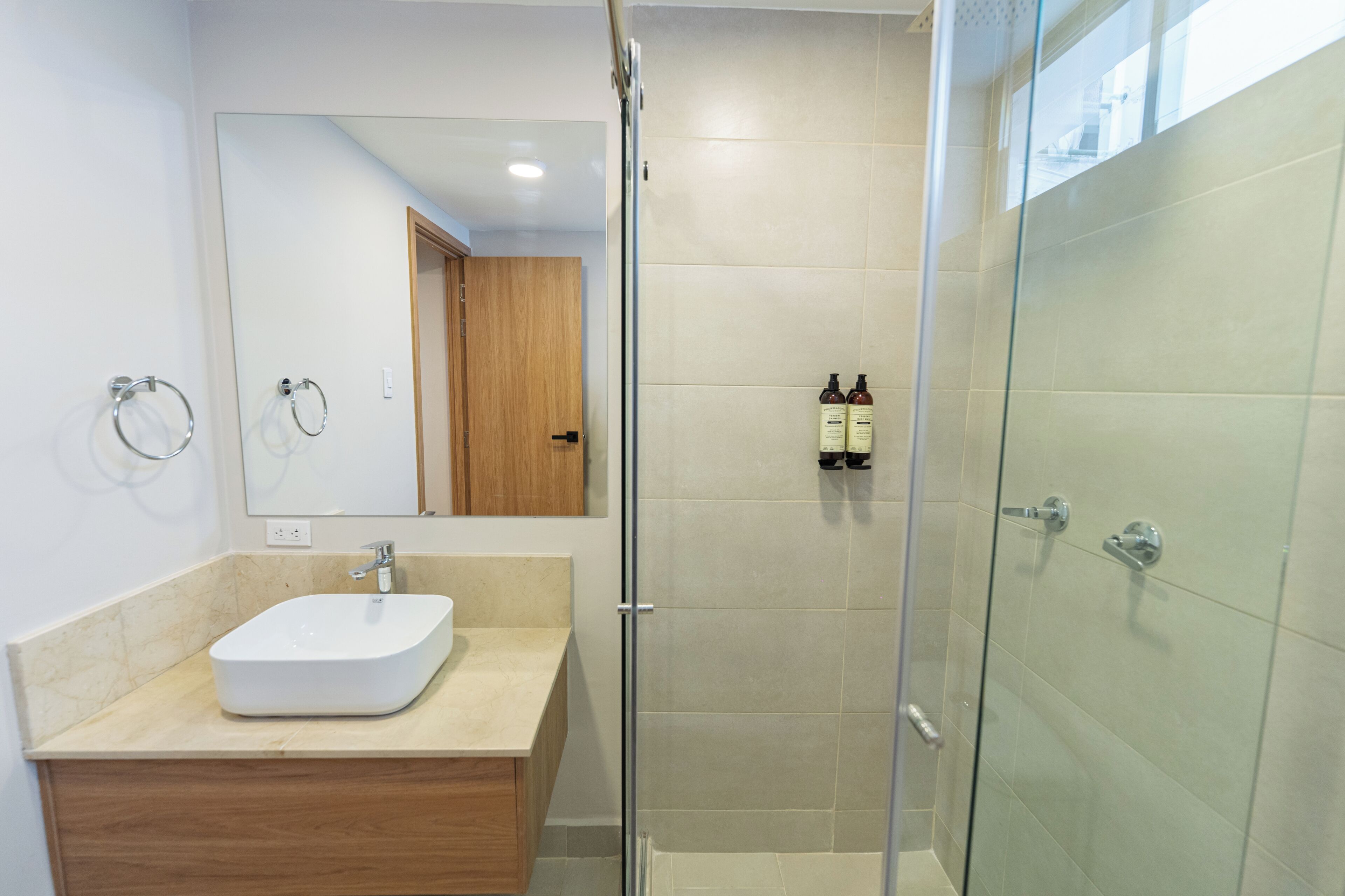 A modern bathroom with a glass-enclosed shower, a wooden vanity, and a large mirror.
