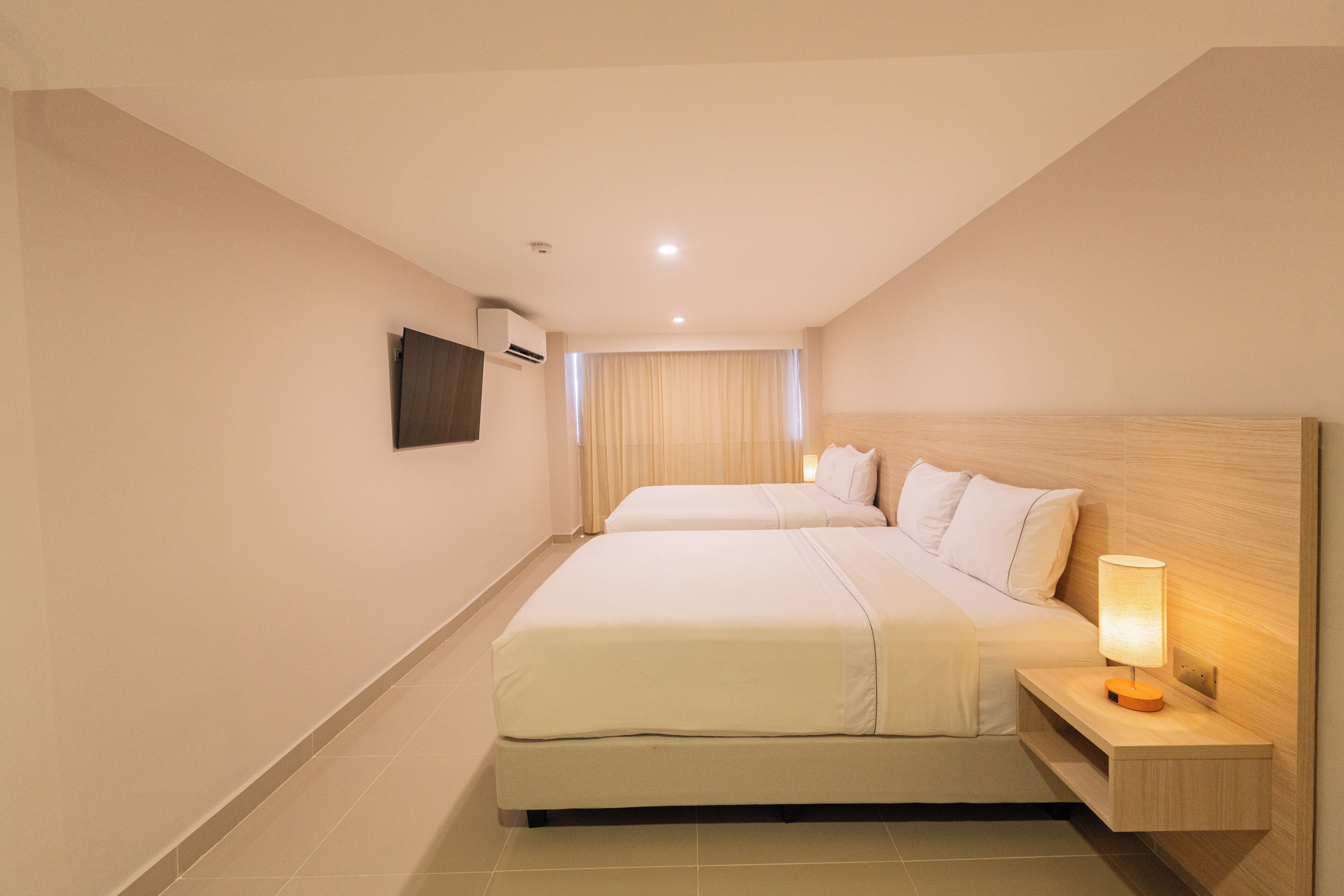 A hotel room with a large bed, a bedside table with a lamp, and a wall-mounted air conditioning unit.