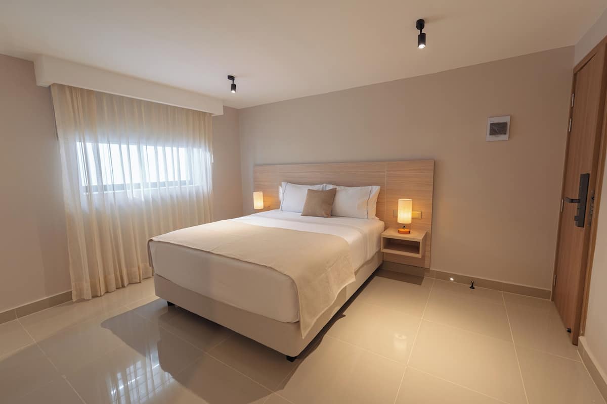 A hotel room with a large bed, bedside lamps, a wooden headboard, and a door.
