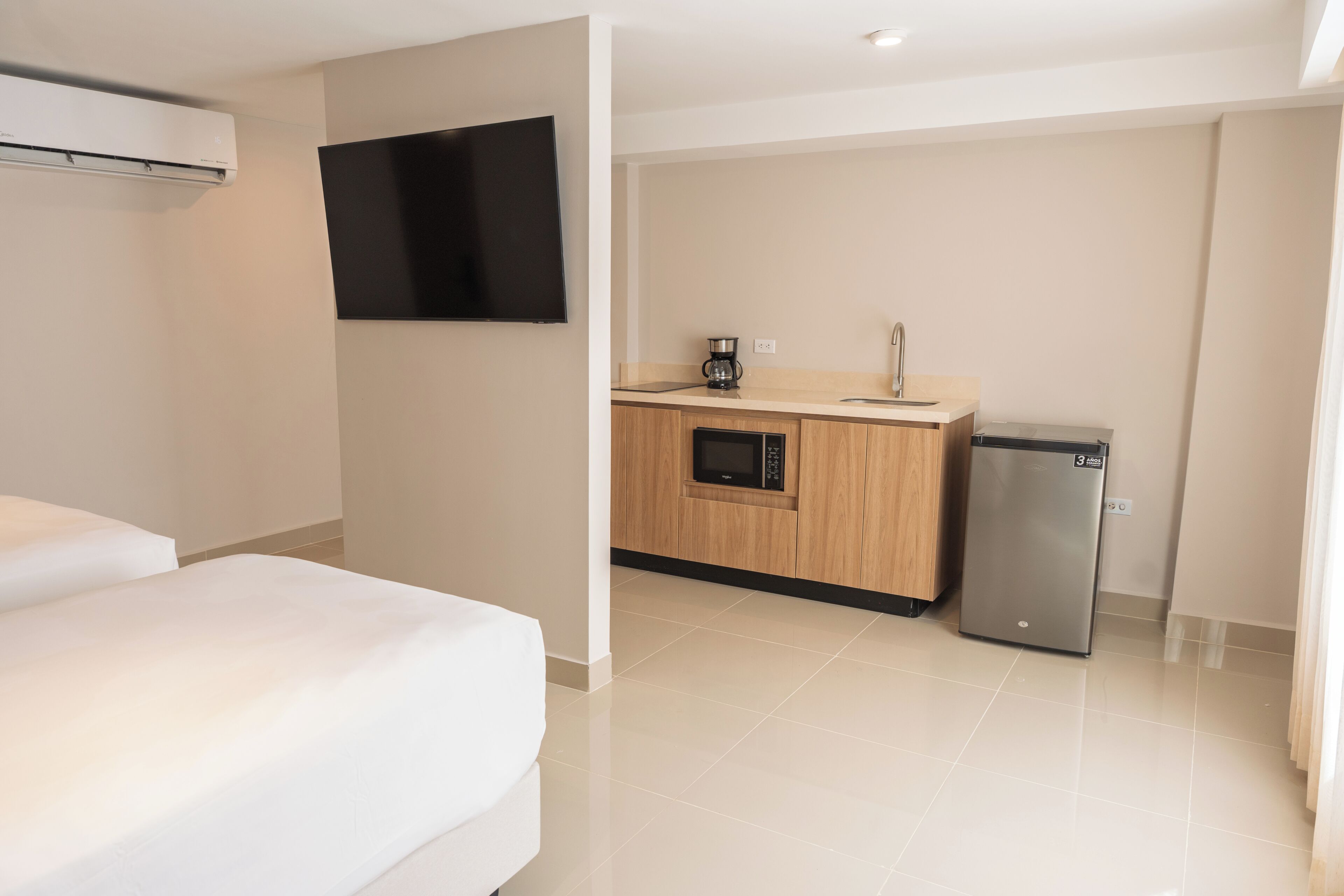 A hotel room with a bed, a kitchenette with a microwave, a coffee maker, and a refrigerator.