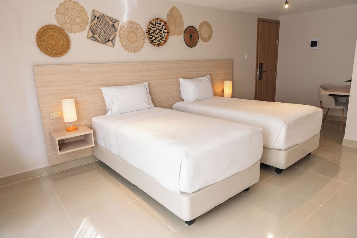 A hotel room with two beds, a wooden headboard, a bedside table with a lamp, and wall decor.